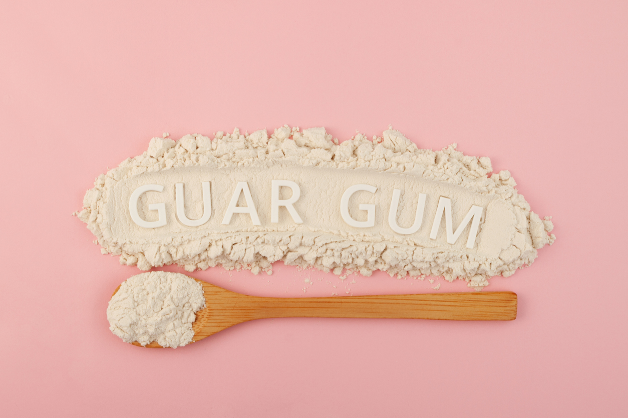 Pulbere de gumă de guar sau guaran în lingură de lemn pe fundal roz, vedere de sus.