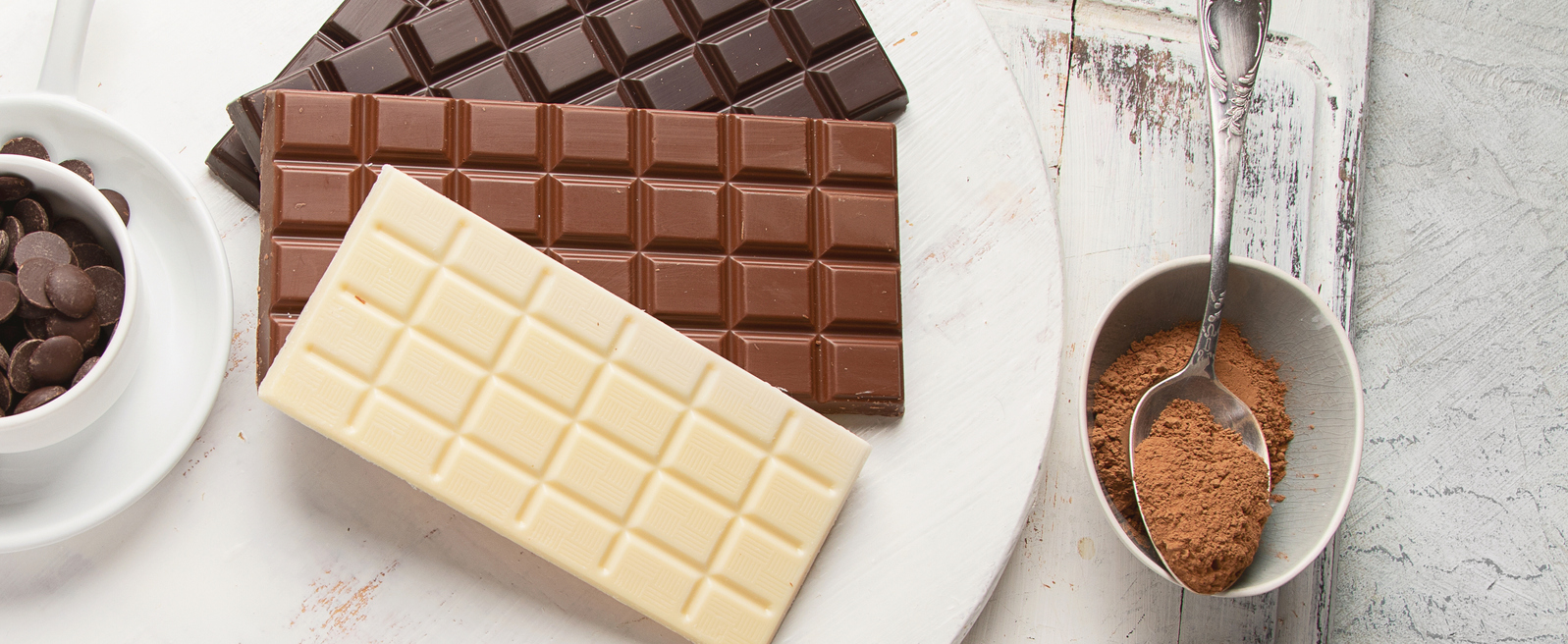 tablete de ciocolata alba, neagra , cu lapte , un bol cu banuti ciocolata si un bol cu cacao