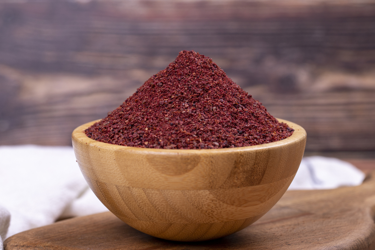 Sumac pe fundal din lemn. Condimente uscate de pudră roșie de sumac măcinate într-un castron de lemn.