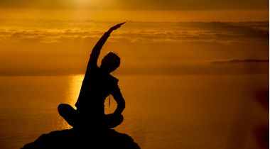 barbat care face yoga pe o stanca la malul marii la apus