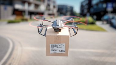 O dronă de livrare zboară între clădiri rezidențiale