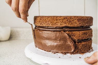 Bucătar de patiserie care răspândește cremă de ciocolată pe marginile unui tort de ciocolată în interior