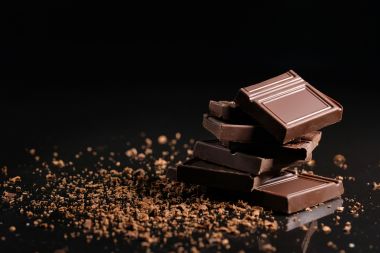Bucăți rupte de ciocolată cu pudră de cacao pe fond negru.
