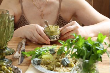 femeie care tine un borcan de pasta de masline verzi si o farfurie cu paste si masline verzi