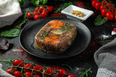 Carne aspic într-o farfurie întunecată cu muștar. Fundal negru.