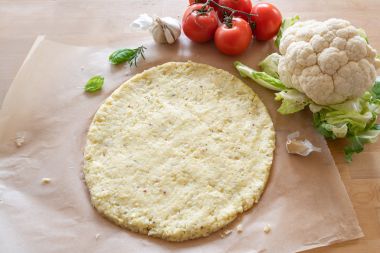 Bază de pizza crudă din conopidă mărunțită pe hârtie de copt, alternativă vegetală sănătoasă pentru dieta