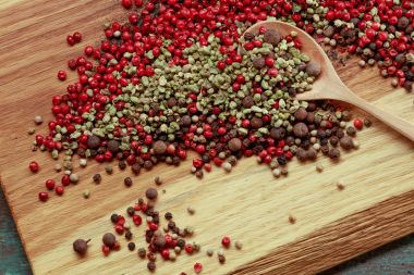Sortiment de boabe de piper împrăștiate într-o lingură și o placă de lemn