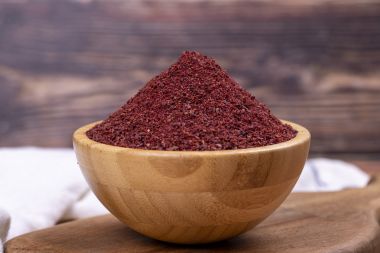 Sumac pe fundal din lemn. Condimente uscate de pudră roșie de sumac măcinate într-un castron de lemn.