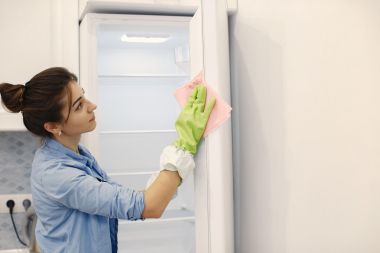 Femeie cu burete și mănuși de cauciuc care curăță frigiderul