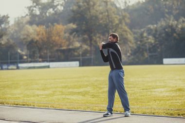 barbat care face intinderi pe un teren de sport