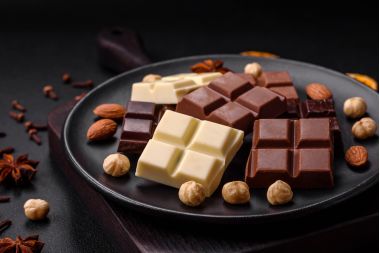 Un amestec de mai multe tipuri de ciocolată dulce delicioasă ruptă în cuburi pe o farfurie neagră