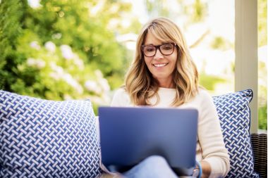 femeie care lucreaza pe laptop in casa ei, pe canapea