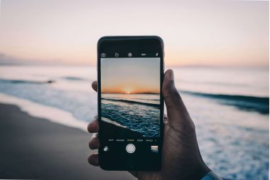 barbat care face poza cu telefonul unui peisaj la malul marii