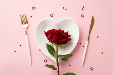 farfurie in forma de inima, cu tacamuri alaturi si un trandafir rosu asezat pe farfurie