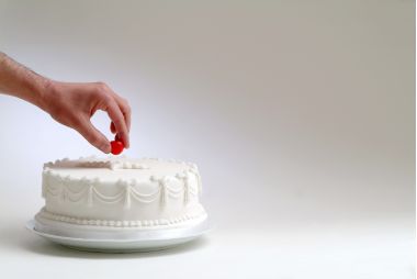 mana de femeie care pune cireasa pe un tort alb