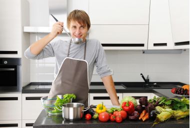 barbat in bucatarie care gateste. Blat de lucru plin cu legume